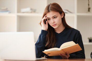 Thinking, A beautiful caucasian female student is studying remotely. She is sitting at a table at home with a laptop and a notepad and concentrated is watching a video conference.