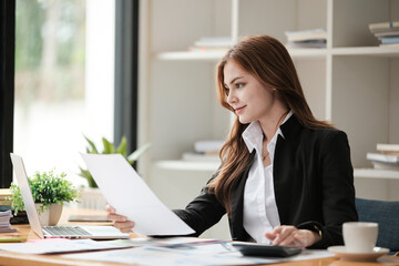Asian Business woman using calculator and laptop for doing math finance on an office desk, tax, report, accounting, statistics, and analytical research concept 
