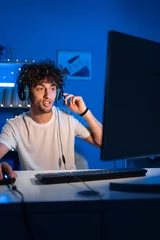 Fotobehang Gaming Positive arabic guy gamer streams game on computer and looks smiling at the camera. Smiling gamer playing video games  © Andrii Lysenko