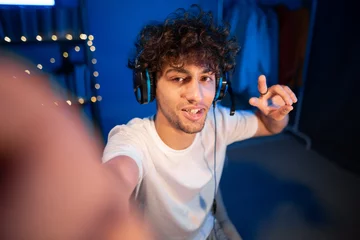 Fototapete Gaming Arabic guy gamer taking selfie and video call with friends, showing victory sign, winning the game  © Andrii Lysenko