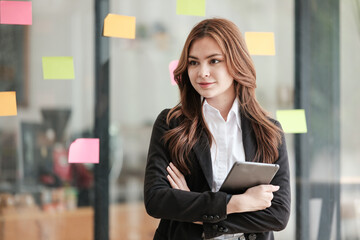 Successful businesswoman standing in creative office and looking at camera. Woman entrepreneur in a co-working space smiling. Portrait of beautiful business woman standing.