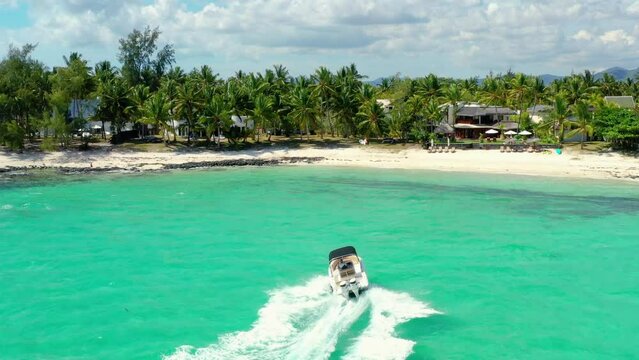Drone shot approaching the palm trees and houses on a stunning beach.