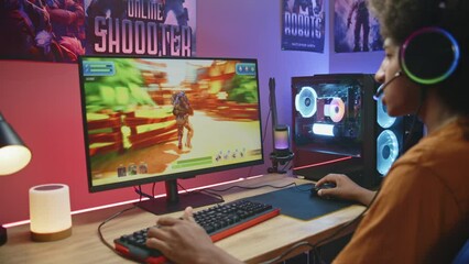 African American gamer talks with teammates and plays in third person shooter on computer at home. Online video game live stream or cybersport championship. Teenager spending leisure time. Dolly shot.
