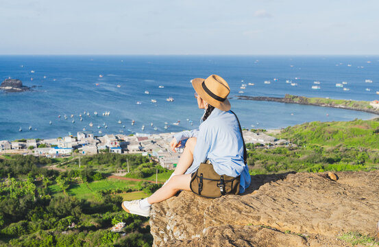 image of a girl sitting on a mountain looking down at the sea