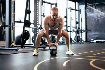 Fit and muscular man focused on lifting a dumbbell during an exercise class in a gym.