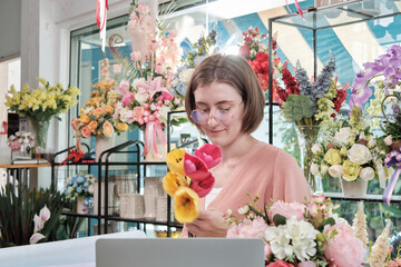 A young White Asian female florist entrepreneur blossoms arranging, decorating, happy work in colorful flower shop store with blooms, and small business owner.