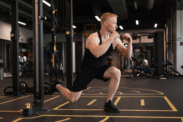 Fototapeta na wymiar Strong sportsman doing bulgarian lunges in a gym with TRX.