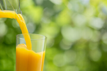 orange juice pouring into glass from jug on green background