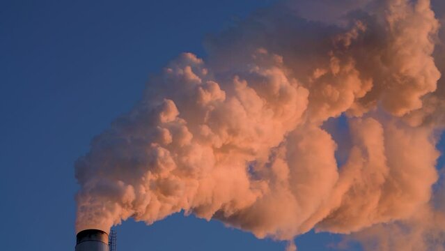 Hot Glowing colorful Smoke Plume sunlit while emitting Greenhouse gas into atmosphere during late evening from Paper mill Industry at Pitea Sweden.