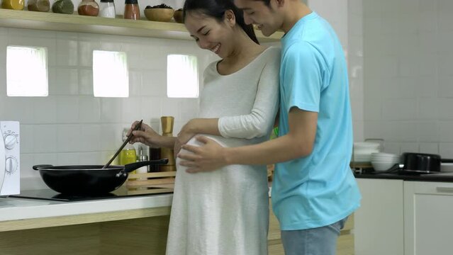 Pregnant wife and man cooking food for breakfast in kitchen at home. Family people prepare meal for eating together.