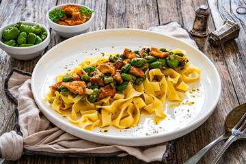 Tagliatelle with broad bean and chanterelle mushrooms on wooden table
 - obrazy, fototapety, plakaty