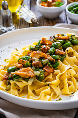 Tagliatelle with broad bean and chanterelle mushrooms on wooden table
