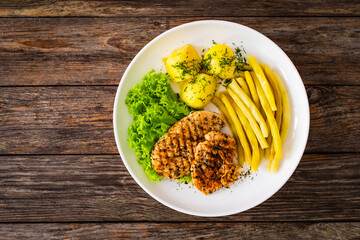 Top-down shoot of grilled chicken breasts with yellow beans and boiled potatoes on wooden table

