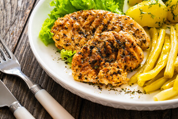 Grilled chicken breasts with yellow beans and boiled potatoes on wooden table
