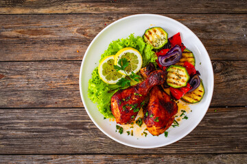 Roasted chicken drumsticks with lettuce and grilled sliced vegetables on wooden table
