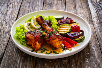 Roasted chicken drumsticks with lettuce and grilled sliced vegetables on wooden table
