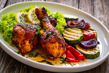 Roasted chicken drumsticks with lettuce and grilled sliced vegetables on wooden table
