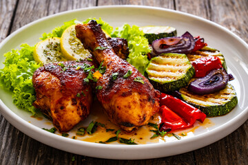 Roasted chicken drumsticks with lettuce and grilled sliced vegetables on wooden table
