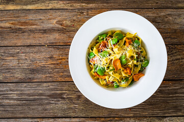 Tagliatelle with broad bean, chanterelle mushrooms and parmesan cheese on wooden table
