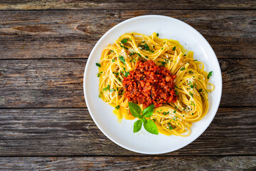 Top-down shoot of linguine with minced pork meat in tomato sauce  with parmesan cheese and basil leaves served on wooden table
