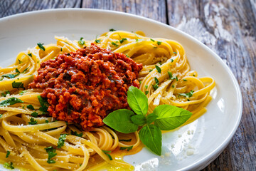 Linguine with minced pork meat in tomato sauce  with parmesan cheese and basil leaves served on wooden table
