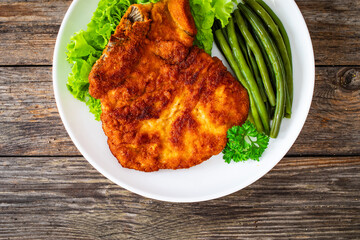 Breaded fried pork chop with cooked green beans on wooden table
