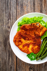 Breaded fried pork chop with cooked green beans on wooden table
