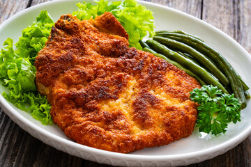 Breaded fried pork chop with cooked green beans on wooden table
