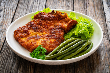 Breaded fried pork chop with cooked green beans on wooden table

