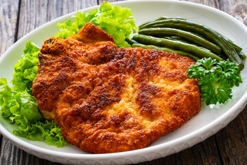 Breaded fried pork chop with cooked green beans on wooden table
