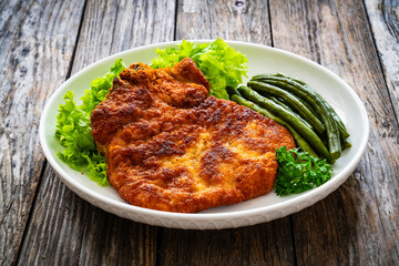 Breaded fried pork chop with cooked green beans on wooden table
