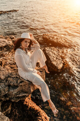 woman sea sunset. woman in a white pantsuit and hat is sitiing on the beach enjoying the sea. Happy summer holidays
