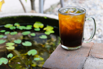 tea in a glass with ice beside a small pond.