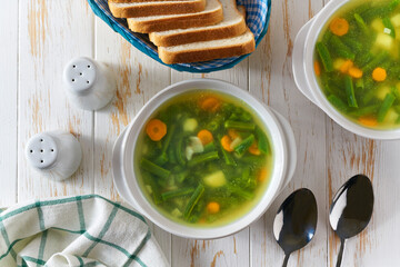 Green soup with potato, green bean and carrot in a white plate on wooden background, top view.
