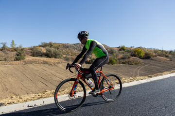 Fototapeta premium Cyclist riding bicycle on road against clear sky