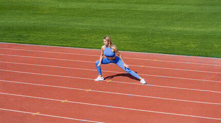 Fototapeta premium Sports exercises and stretching in the stadium. Physical training girl. Fit girl do outward lunging. Physical training education. Sports lesson. Female runner stretching before workout