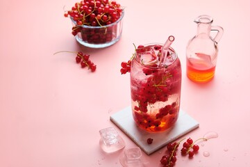 Soft drink, water with ice, syrup and red currant berries in a glass on a pink plain background. Summer drinks. Photo in one color