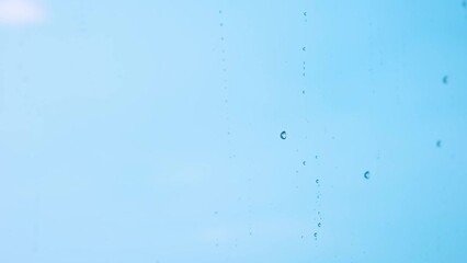 Raindrops falling on the transparent glass on a blue background give a feeling of coldness and loneliness.