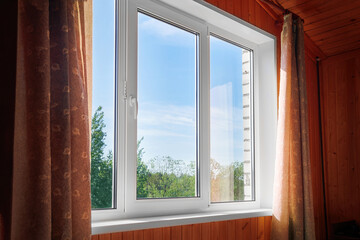 Closed plastic window and wall inside the room. Window with view of summer sunny backyard of wooden country house.