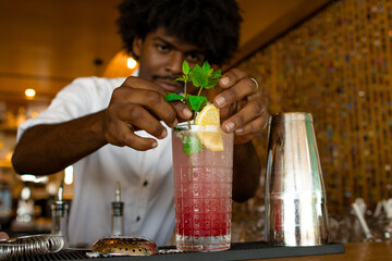 latin bartender with curly hair putting a top of mint in the cocktail