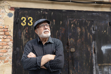 charismatic elderly man in glasses and a cap standing on the background of an old garage door with the number 33, horizontal format