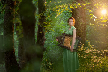 girl r in a green long dress stands in the forest with an antique mirror