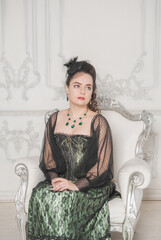 Beautiful young smiling woman wearing green medieval vintage Victorian Style dress in the armchair