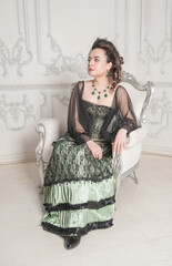 Beautiful young woman wearing green medieval vintage Victorian Style dress sitting in the armchair