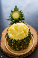 fresh pineapple smoothie in pineapple fruit cup on wooden saucer and black wood table for sweet fruit juice or citrus cold drink and healthy detox to diet beverage in cafe shop or restaurant on summer