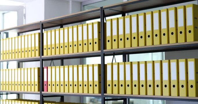 Red folder moves on shelves in row of identical yellow ones in archive. Storage of business documents