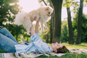 A young woman lies on the grass and holds her Pomeranian dog in her arms.