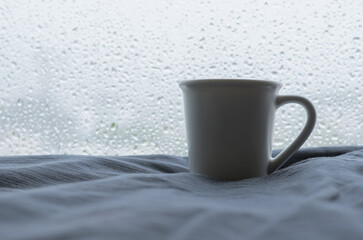 A cup of Espresso coffee shot puts on bed with rain drop on window in raining day. Stay home concept.