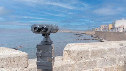 tourist binoculars in front of the ramparts of Alghero and Capo Caccia in the distance
