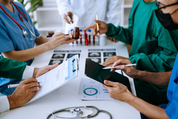 Medical team having a meeting with doctors in white lab coats and surgical scrubs seated at a table discussing a patients working online using computers
